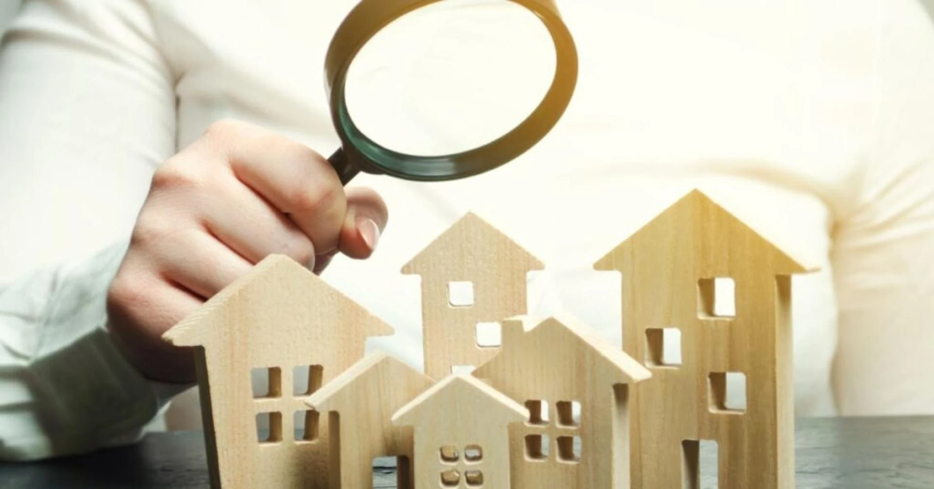 A woman is holding a magnifying glass over a wooden houses Real estate appraiser Property valuation appraisal Find a house Search for housing Real estate market analysis Selective focus